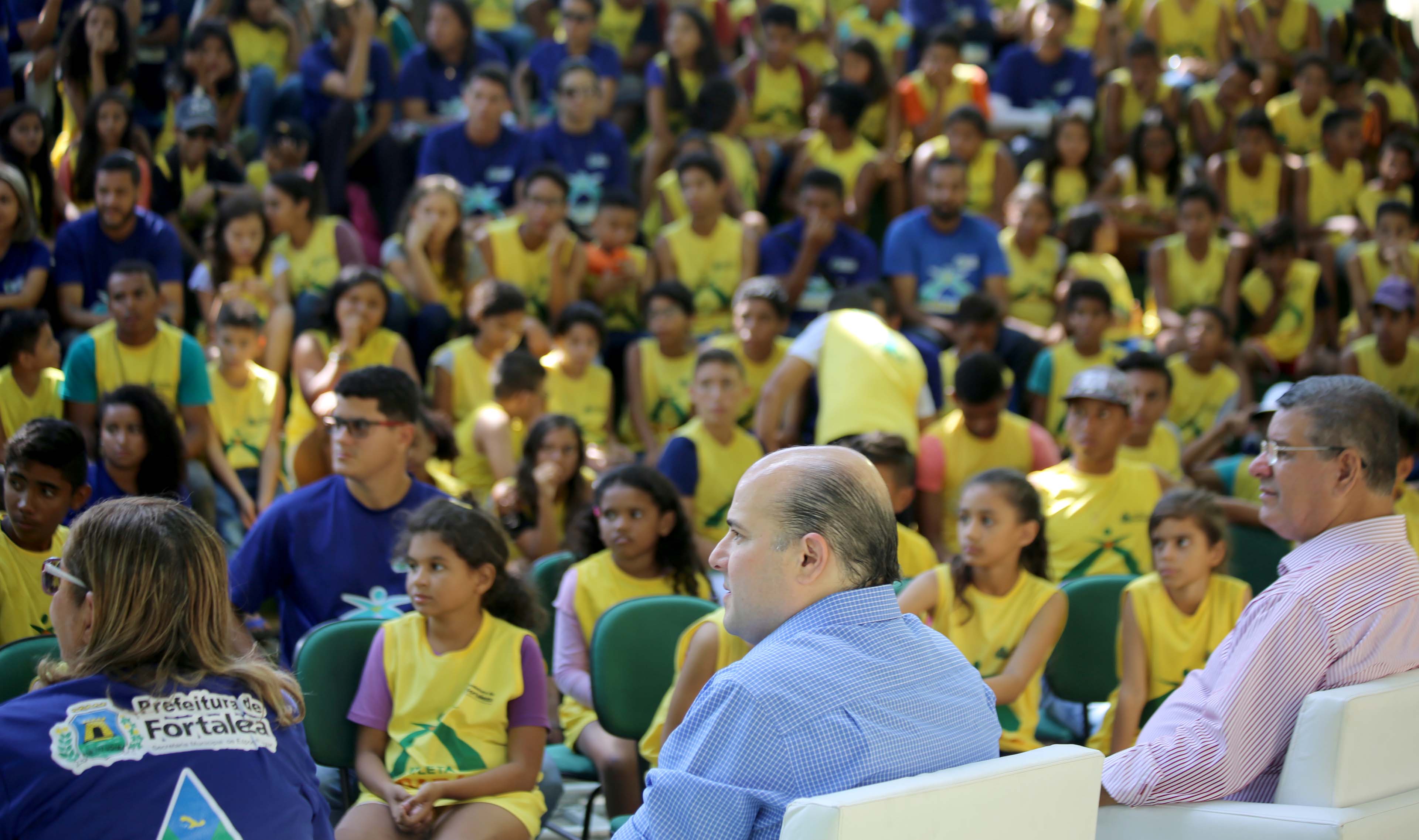 prefeito roberto cláudio sentado na frente de dezenas de pessoas num palco 
